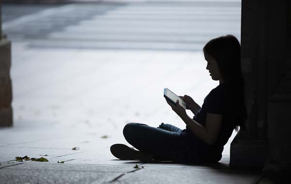 Girl using tablet sat on floor outside silhouetted