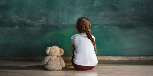 child staring at empty blackboard with teddy by her side